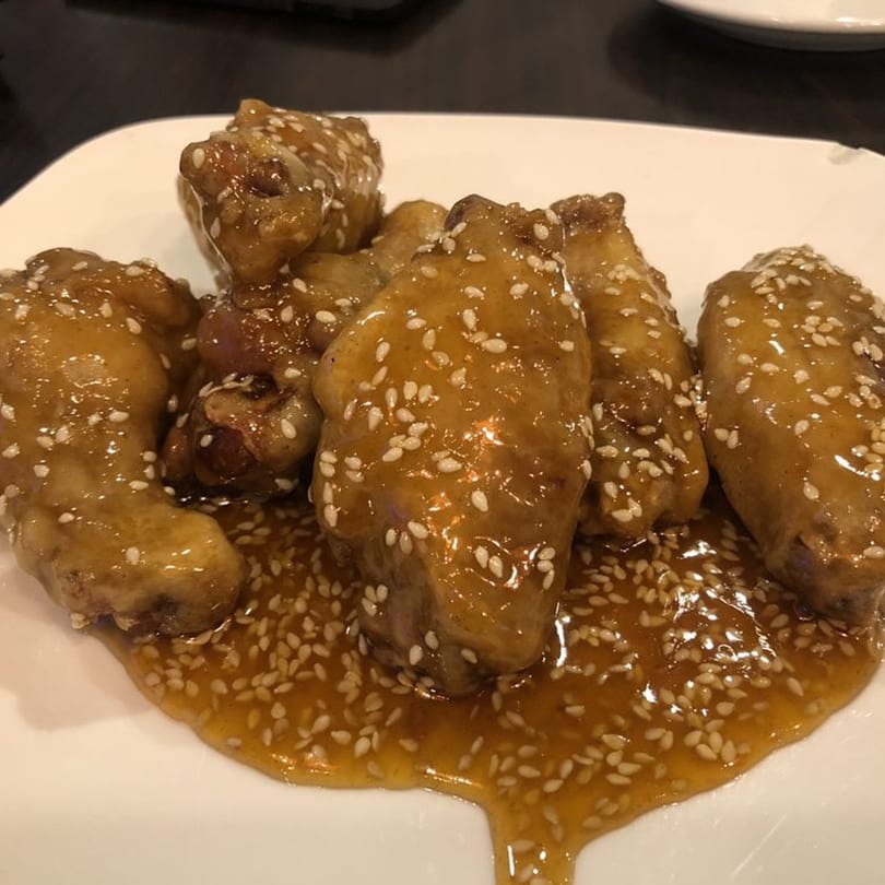 Boulder Pho's sesame chicken wings, glistening with sauce and sprinkled with sesame seeds on a white plate.