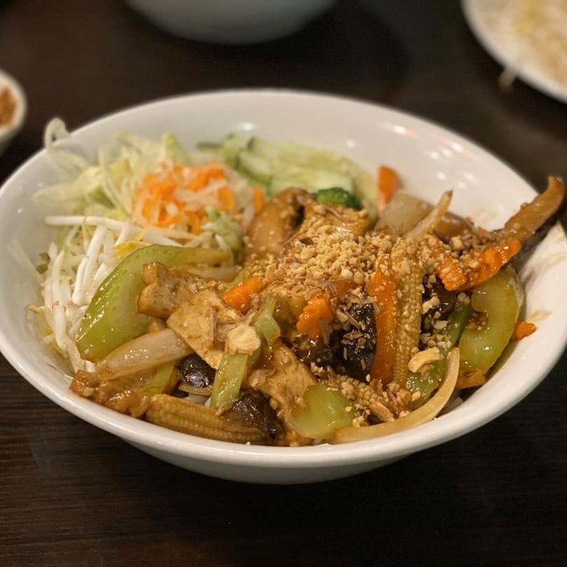 A white bowl of Vietnamese stir-fried vegetables, tofu, and peanuts, with a side of shredded cabbage and carrots.