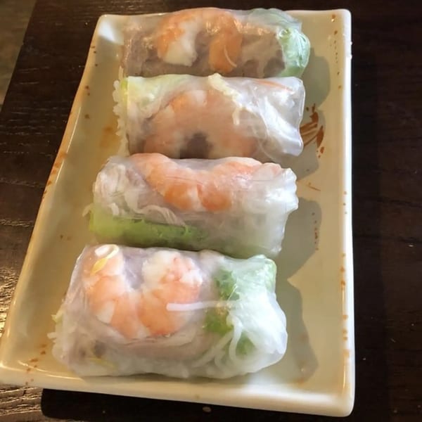 Four fresh Vietnamese spring rolls with shrimp, noodles, and greens on a rectangular plate.