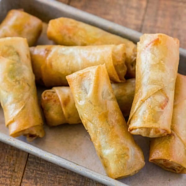 Golden-brown crispy egg rolls are arranged on a metal tray, ready to be served.